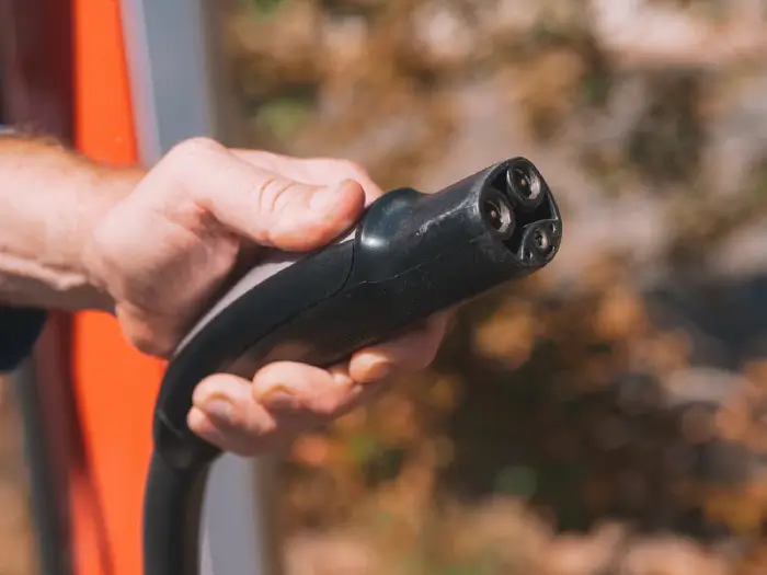 Free Hand holding an electric vehicle charging plug, symbolizing clean energy and innovation. Stock Photo