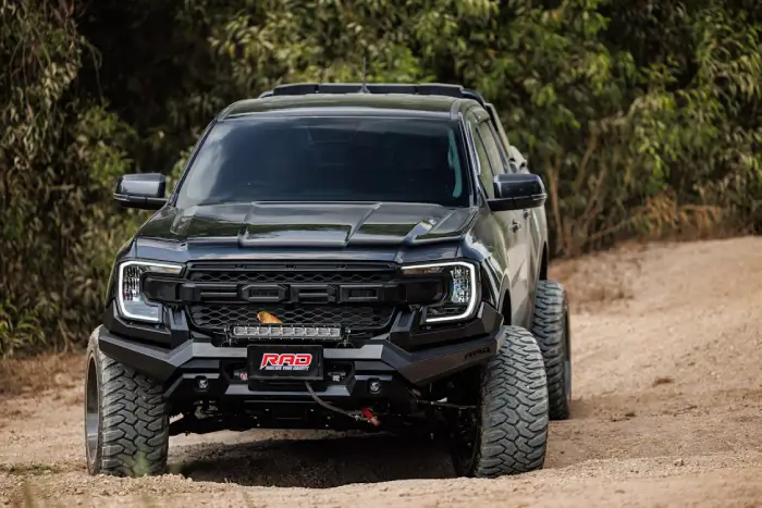 Free High-performance black off-road truck driving through a rugged dirt path amidst lush greenery. Stock Photo