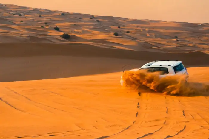 Free A thrilling SUV driving through the sand dunes of Dubai's desert landscape at sunset. Stock Photo