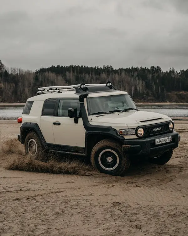 Free Modern SUV car driving on wild sandy beach near lake and lush green trees against gray cloudy sky Stock Photo